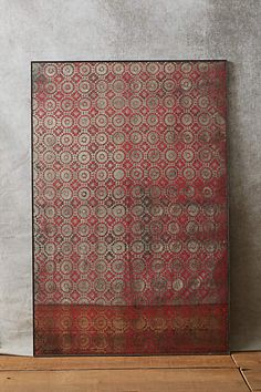 an old red and black rug sitting on top of a wooden floor next to a vase