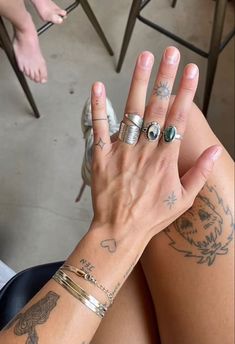 a woman's hands with tattoos and rings on her left arm, sitting at a table