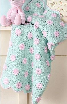 a crocheted baby blanket with pink flowers on it and a teddy bear sitting next to it