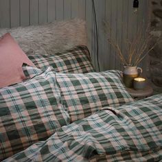 a bed with green and white checkered comforter next to a table with candles on it