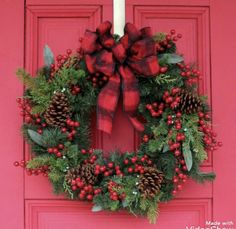 a christmas wreath on a red door with pine cones and berries hanging from the front