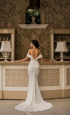 a woman standing in front of a counter wearing a white dress and looking off to the side