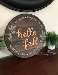 a wooden sign that says hello fall on the side of a wall next to a potted plant