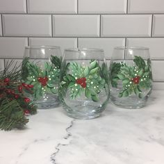 three wine glasses decorated with holly leaves and red berries are sitting on a marble countertop