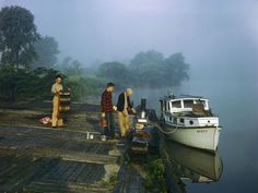 three people standing on a dock next to a small boat in the foggy water