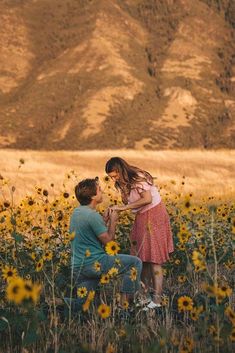 a man kneeling down next to a woman in a field of sunflowers