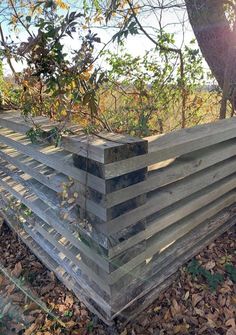 a stack of wooden boards sitting on top of leaf covered ground next to a tree