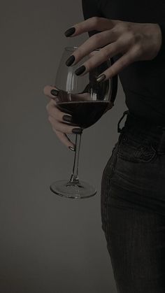 a woman holding a wine glass in her right hand and wearing black nail polishes