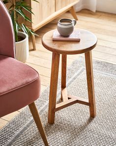 a small table with a cup on it next to a pink chair and potted plant