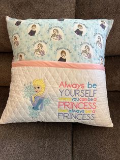 a pillow with princesses on it sitting on a couch in front of a brown sofa