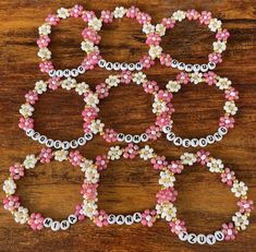 several pink and white beaded bracelets sitting on top of a wooden table