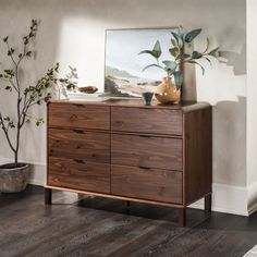 a wooden dresser sitting in a living room next to a painting and potted plant