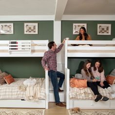 three people are sitting on bunk beds in a room with green walls and white furniture