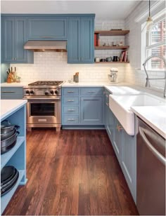 a kitchen with blue cabinets and white counter tops, wooden flooring and stainless steel appliances