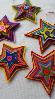 five brightly colored star shaped ornaments on a white tablecloth with string and thread spools