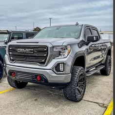 the front end of a silver truck parked in a parking lot next to other trucks