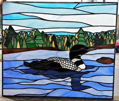 a stained glass panel depicting a duck swimming in the water with trees and mountains in the background