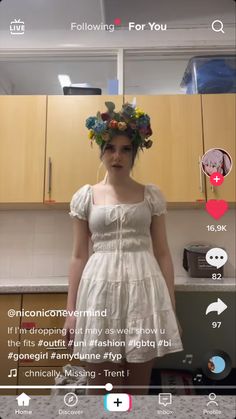 a woman wearing a flower crown standing in front of a kitchen counter with wooden cabinets