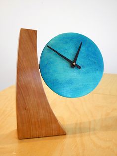 a blue clock sitting on top of a wooden table next to a piece of wood