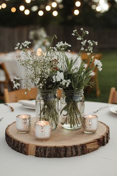 Mason jar wedding centerpiece on a rustic log slice with flowers and candles, perfect for an outdoor or barn wedding. Rustic Modern Wedding Centerpieces, Small Table Centerpiece Ideas, Minimalist Country Wedding, Barn Style Wedding Decor, Simple Barn Wedding Decorations, Simple Boho Centerpieces Wedding, Woodsy Wedding Centerpieces, Simple Outdoor Wedding Reception, Simple Rustic Wedding Centerpieces