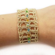 a close up of a person's arm wearing a gold bracelet with multi colored stones