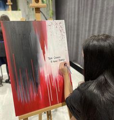 a woman is painting on an easel with red and black paint