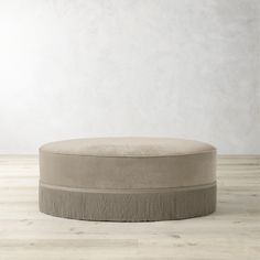 a round ottoman sitting on top of a hard wood floor next to a white wall