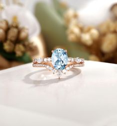 a ring with an oval blue topaz surrounded by smaller round diamonds on a white surface