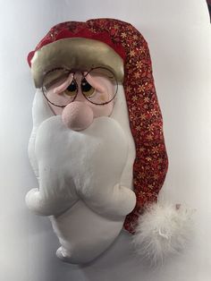 a stuffed santa clause wearing glasses and a red hat on top of a white wall