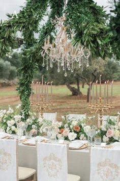 a table set up with white linens and greenery for an outdoor wedding reception