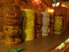 several tiki mugs are lined up on a shelf