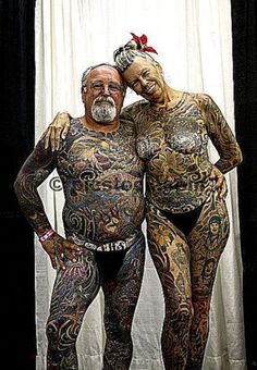 an older man and woman standing next to each other with tattoos on their bodys