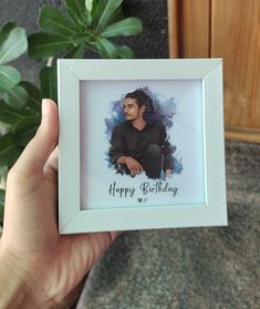 a person holding up a birthday card in front of a plant