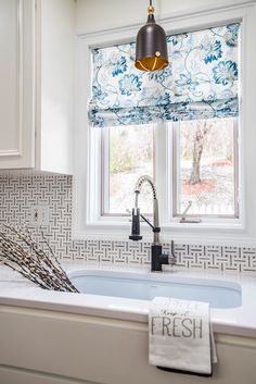 a kitchen sink under a window next to a faucet and counter top with blue flowers on it