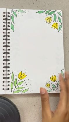 a person holding a pen and looking at a notebook with yellow flowers on the pages