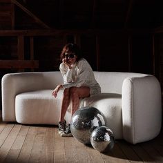 a woman sitting on a white couch next to two shiny disco balls in front of her