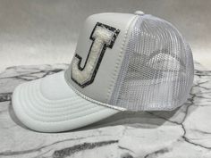 White Foam Trucker Cap with WHite Varsity Chenille Letter "J" outlined in silver glitter. Chenille Swag Varsity Letter Swag Foam Trucker OTTO Cap - 5 panel Mid Profile Mesh Back, Custom Monogram, Initial Hat, Bachelorette Gift. Cheap Snapback Hat With Letter Print, Cheap Trucker Hat With Letter Patch Snapback, Cheap Gray Trucker Hat With Letter Print, Bachelorette Gift, Varsity Letter, Hats Snapback, Bachelorette Gifts, Letter J, White Letters