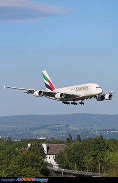 an airplane is taking off into the sky over some trees and hills in the background