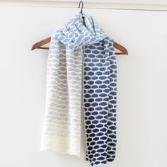 two scarves hanging on a wooden hanger in front of a white wall with blue and white designs