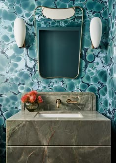 a bathroom vanity with marble counter top and gold faucet, against a blue floral wallpaper