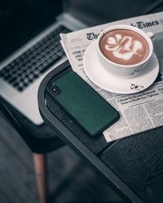 a cup of coffee sitting on top of a table next to a cell phone and newspaper