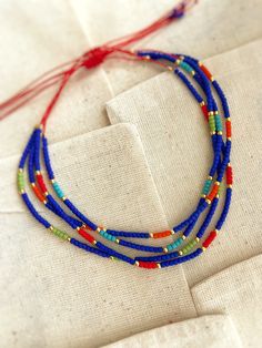 three strand beaded necklace with red, green and blue beads on white fabric background