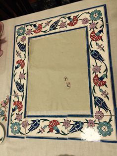 a mirror sitting on top of a table covered in blue and red flowers next to a cup