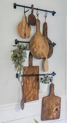 several wooden cutting boards hanging on a wall with potted plants and utensils