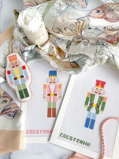 two cross - stitch patterns are on the table next to some fabric and other items