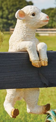 a stuffed sheep sitting on top of a wooden fence next to a green grass covered field