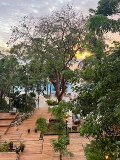 a wooden walkway with benches and trees on the other side, leading to an outdoor swimming pool