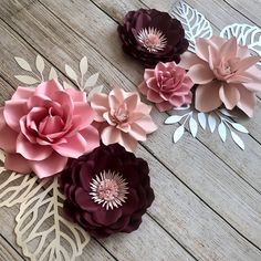 three paper flowers are laying on a wooden surface, one is pink and the other is purple