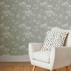 a white chair sitting on top of a rug next to a wall with flowers painted on it