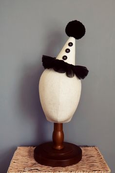 a white mannequin wearing a black and white hat on top of a wooden stand